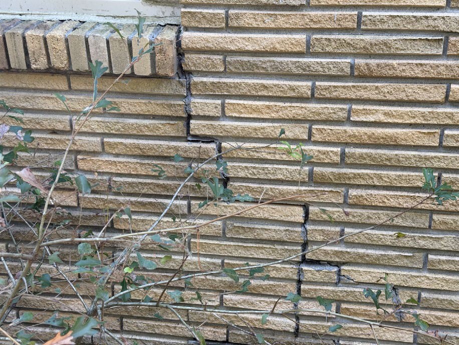 Stepped cracking and previous mortar repairs in exterior brick veneer.