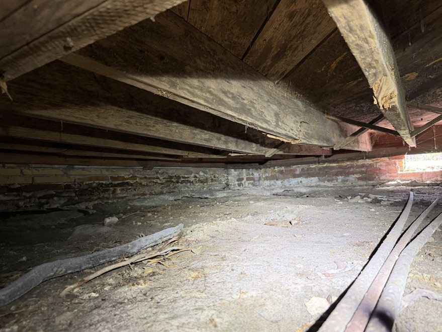 Cracked wooden floor joist with visible deflection beneath a floor in a crawlspace.